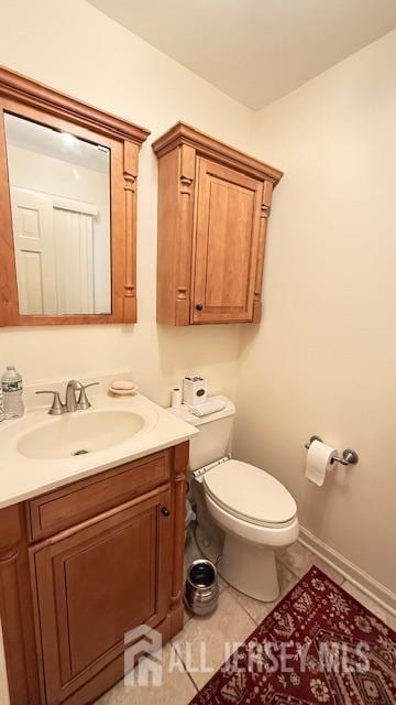 half bathroom with tile patterned flooring, baseboards, vanity, and toilet