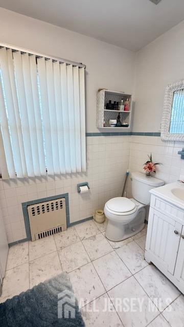 bathroom with tile walls, radiator, toilet, wainscoting, and vanity