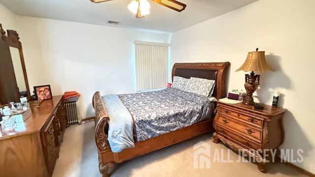 carpeted bedroom with radiator heating unit, visible vents, and ceiling fan