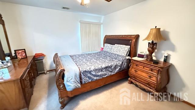 carpeted bedroom featuring radiator, ceiling fan, and visible vents