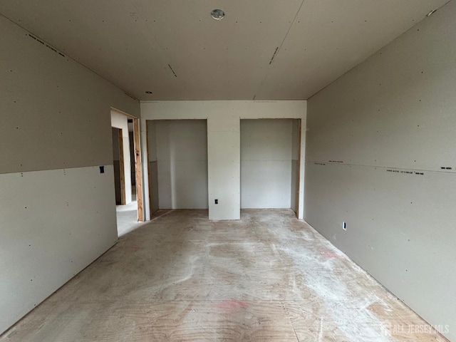 unfurnished bedroom featuring two closets and unfinished concrete flooring