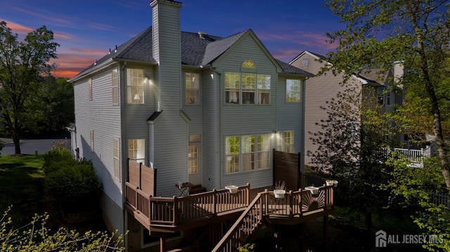 16 Exeter Pass, Colts Neck, NJ 07722 - back of house at dusk featuring a deck, a chimney, and roof with shingles