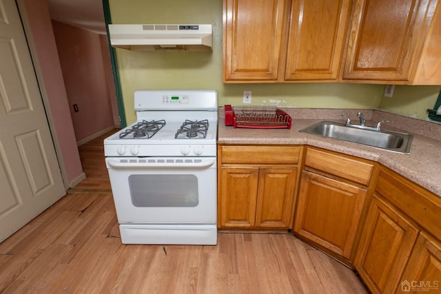 kitchen with light wood-style flooring, white range with gas stovetop, under cabinet range hood, a sink, and light countertops