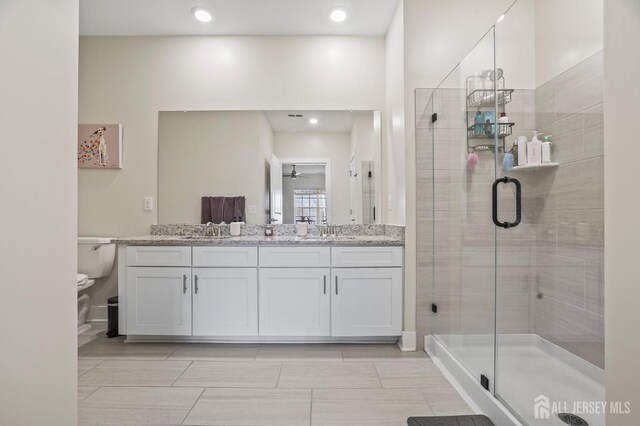 bathroom with a shower with door, vanity, ceiling fan, and toilet