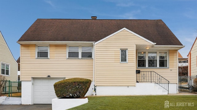 rear view of property with a garage, roof with shingles, fence, and a lawn