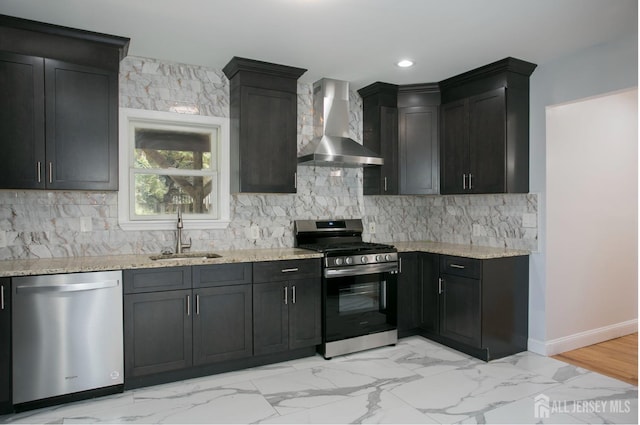 kitchen with light stone counters, a sink, stainless steel appliances, wall chimney range hood, and backsplash