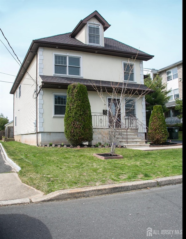 american foursquare style home with a front lawn, a shingled roof, and stucco siding