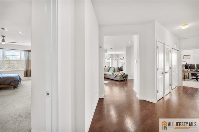 hallway featuring dark wood finished floors, visible vents, and baseboards