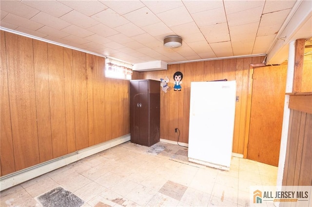 empty room featuring a baseboard heating unit, wood walls, and light floors