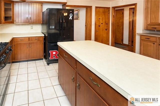 kitchen with light tile patterned floors, brown cabinetry, glass insert cabinets, light countertops, and black appliances