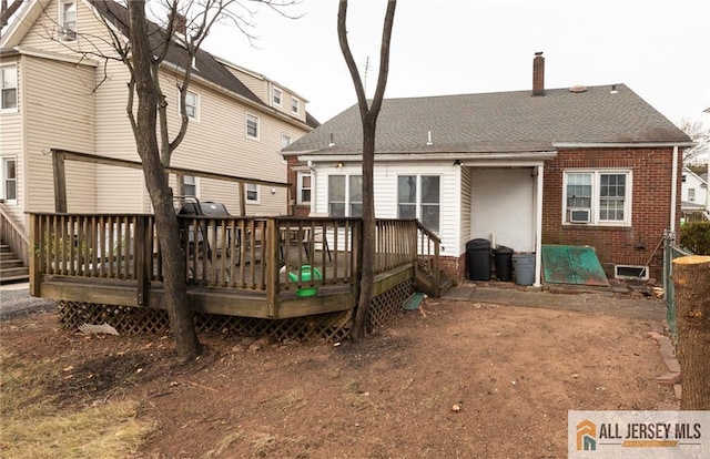 rear view of property featuring roof with shingles, a chimney, a deck, and brick siding