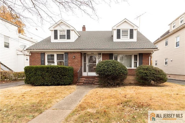 cape cod-style house featuring a shingled roof, entry steps, brick siding, and a front lawn