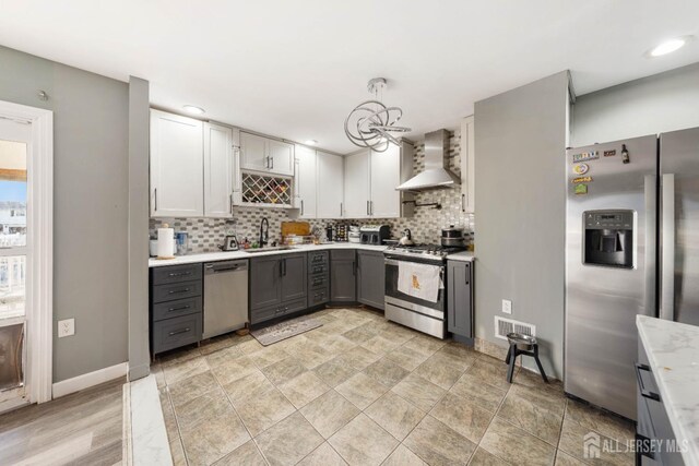 kitchen featuring sink, appliances with stainless steel finishes, gray cabinetry, decorative light fixtures, and wall chimney exhaust hood