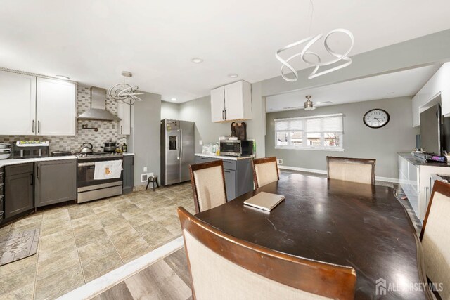 kitchen featuring appliances with stainless steel finishes, decorative light fixtures, white cabinetry, ceiling fan, and wall chimney exhaust hood