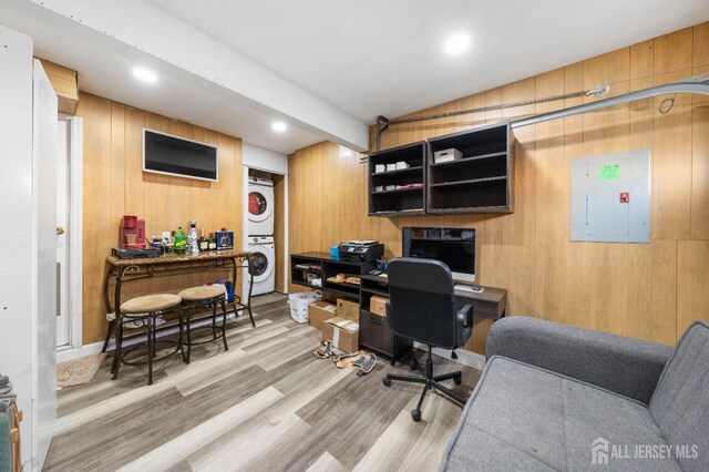 home office with stacked washer and dryer, wooden walls, electric panel, light hardwood / wood-style floors, and vaulted ceiling