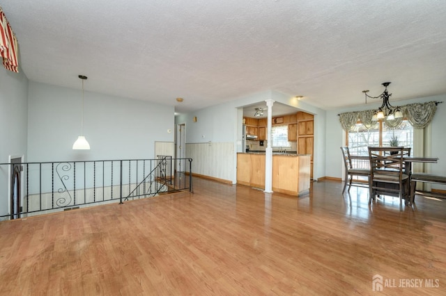 empty room with an inviting chandelier, ornate columns, a textured ceiling, and light wood-type flooring