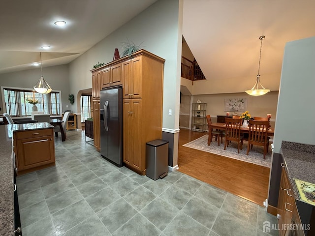 kitchen with brown cabinets, high vaulted ceiling, dark stone counters, stainless steel refrigerator with ice dispenser, and decorative light fixtures