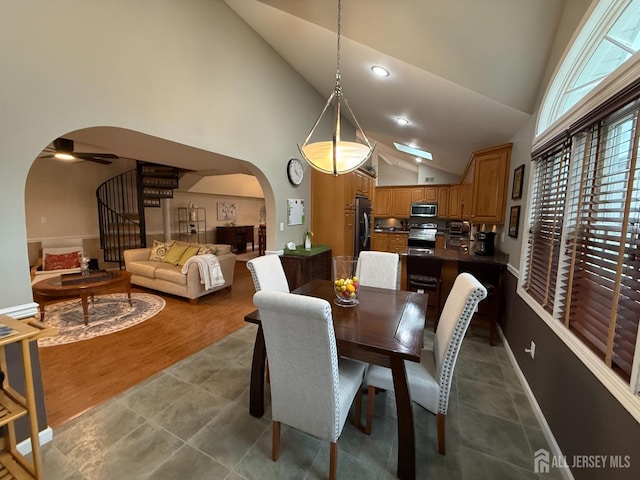 tiled dining space with arched walkways, high vaulted ceiling, stairway, and recessed lighting