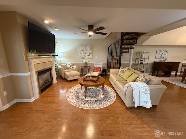 living room with wood finished floors, stairway, a ceiling fan, baseboards, and a tiled fireplace