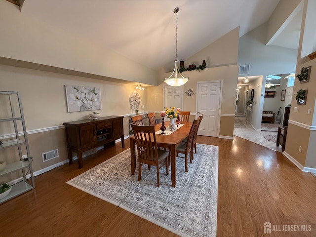 dining room with wood finished floors, baseboards, and high vaulted ceiling