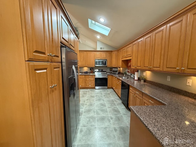 kitchen with a sink, brown cabinetry, vaulted ceiling with skylight, dark stone counters, and appliances with stainless steel finishes