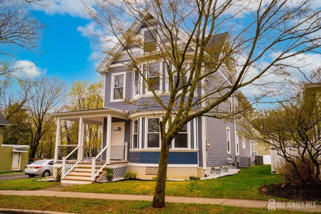 victorian-style house featuring covered porch, a front yard, and central AC unit