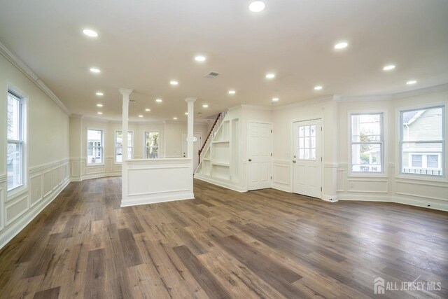 unfurnished living room with dark wood-style floors, decorative columns, ornamental molding, and a healthy amount of sunlight