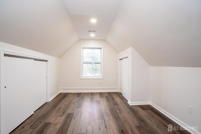 additional living space with baseboards, visible vents, vaulted ceiling, and dark wood finished floors