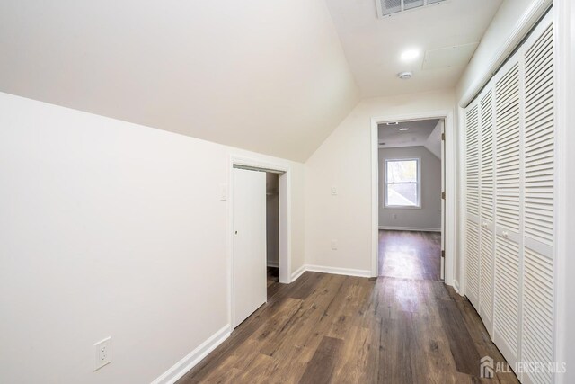 corridor featuring baseboards, dark wood-style floors, visible vents, and vaulted ceiling