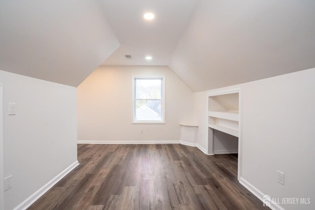 additional living space featuring dark wood finished floors, baseboards, visible vents, and vaulted ceiling