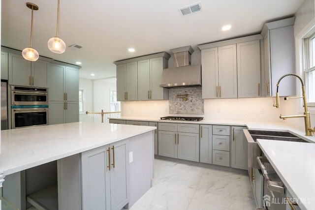 kitchen featuring wall chimney exhaust hood, gray cabinetry, stainless steel appliances, marble finish floor, and visible vents