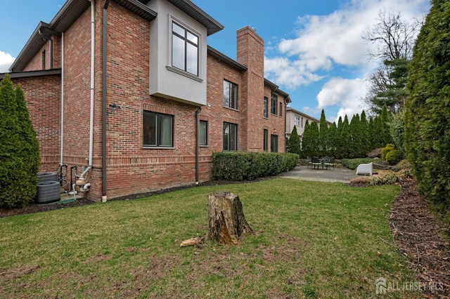 exterior space with a patio, a lawn, a chimney, and brick siding