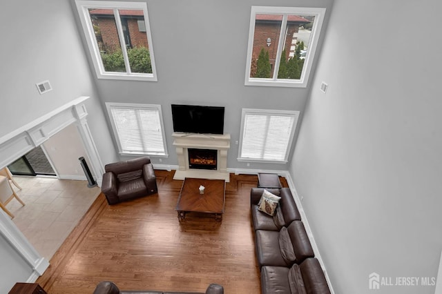 living room featuring baseboards, visible vents, a lit fireplace, and a towering ceiling