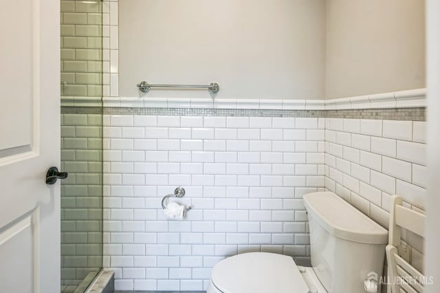 bathroom featuring wainscoting, tile walls, a tile shower, and toilet