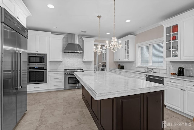 kitchen featuring decorative backsplash, built in appliances, a notable chandelier, and wall chimney range hood
