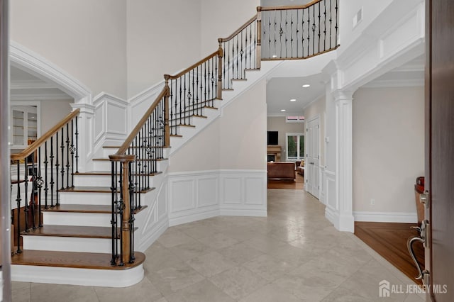 staircase with a towering ceiling, tile patterned floors, ornamental molding, a decorative wall, and ornate columns