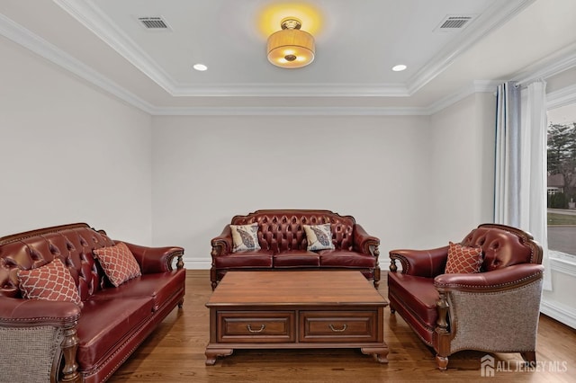 living area featuring ornamental molding, a tray ceiling, wood finished floors, and visible vents