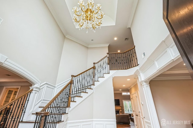 staircase with crown molding, ornate columns, a notable chandelier, a high ceiling, and recessed lighting