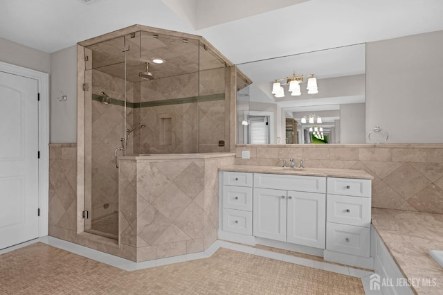 bathroom featuring vanity, an inviting chandelier, tile walls, a wainscoted wall, and a stall shower