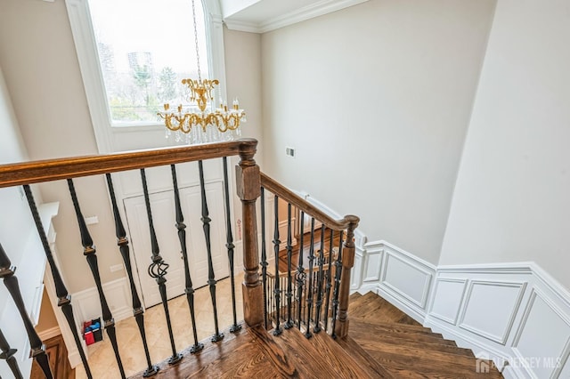 stairs featuring crown molding, wood finished floors, a wainscoted wall, a chandelier, and a decorative wall