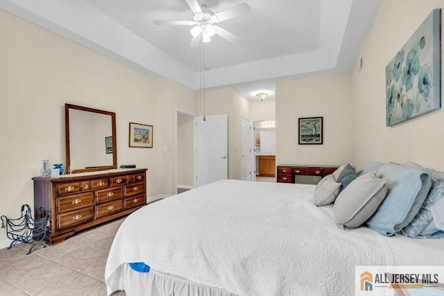 bedroom featuring baseboards, a ceiling fan, a tray ceiling, connected bathroom, and light tile patterned flooring