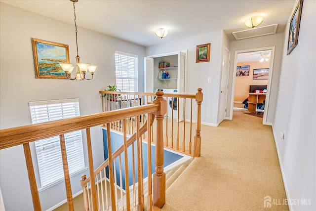 hall with an upstairs landing, light colored carpet, a chandelier, and baseboards