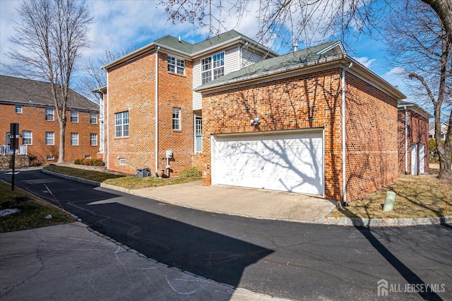view of side of property featuring brick siding, cooling unit, an attached garage, and driveway