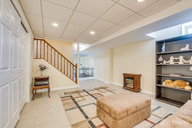 tiled living room with baseboards, stairs, recessed lighting, a glass covered fireplace, and a paneled ceiling