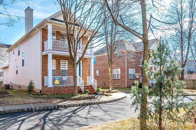 view of front of house with brick siding, central AC unit, covered porch, a chimney, and a balcony