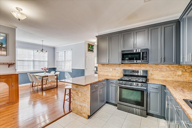 kitchen featuring light tile patterned floors, a peninsula, ornamental molding, appliances with stainless steel finishes, and backsplash