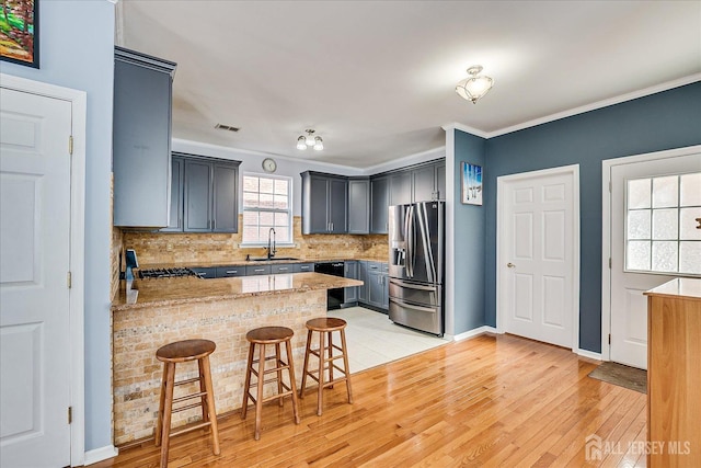 kitchen featuring visible vents, a peninsula, a sink, stainless steel refrigerator with ice dispenser, and tasteful backsplash