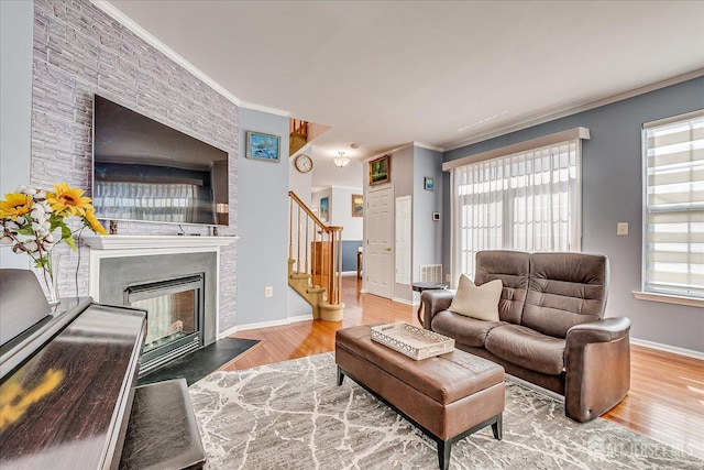 living area with wood finished floors, baseboards, a fireplace with flush hearth, stairs, and crown molding