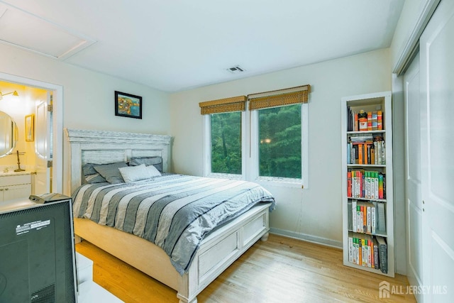 bedroom featuring visible vents, baseboards, light wood-style floors, ensuite bath, and attic access