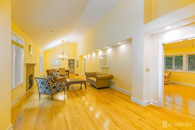 living room with high vaulted ceiling, a stone fireplace, light wood-style flooring, a notable chandelier, and baseboards